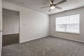 An empty living room with a large window and a ceiling fan